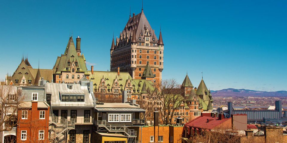 Historic red brick towered building sitting atop a hill surrounded by colorful homes and buildings in Quebec City, Canada.