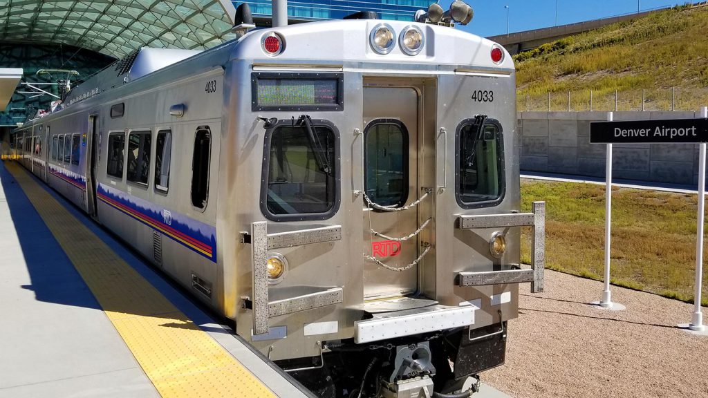 Silver colored intercity train waiting at station platform at Denver airport.