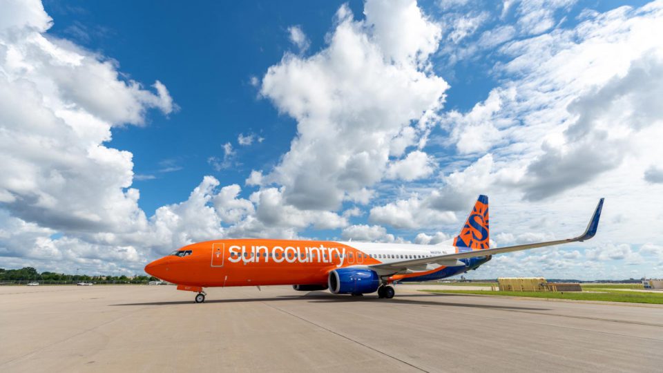 Sun Country's orange, white, and blue Boeing 737 on runway.