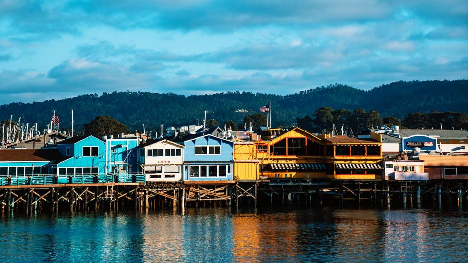 Colorful wooden buildings stand on a wharf along a harbor.