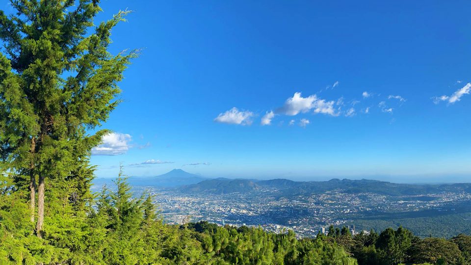 Vibrant green hills against a blue sky with a city in the valley below.