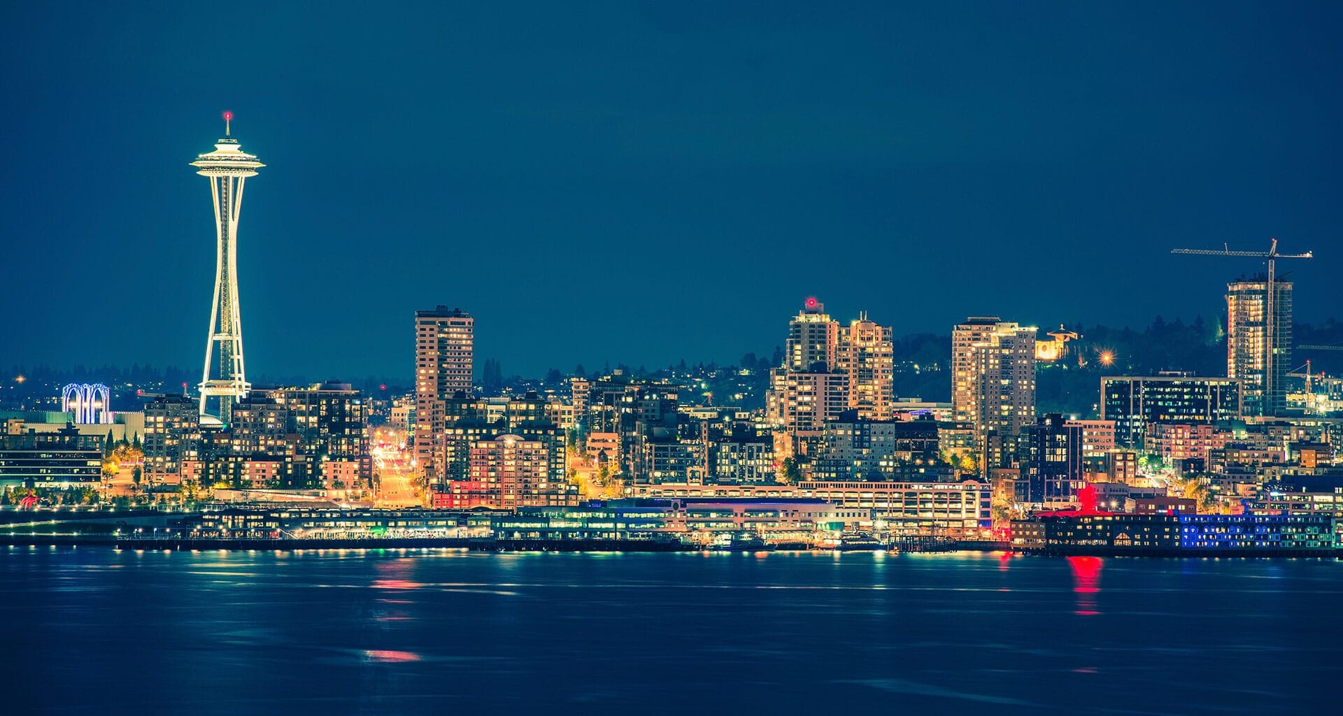 Colorful Seattle skyline reflects on the water at night.